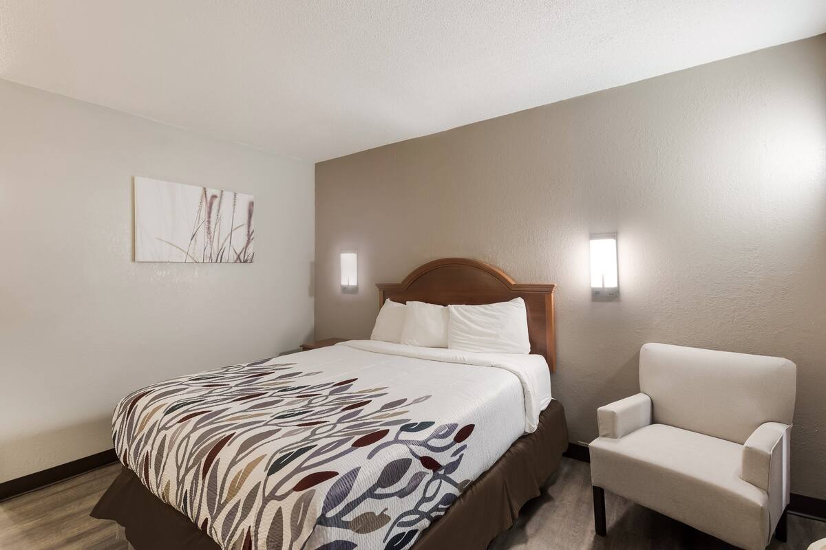 A hotel room with a bed, a chair, and a wall-mounted artwork.