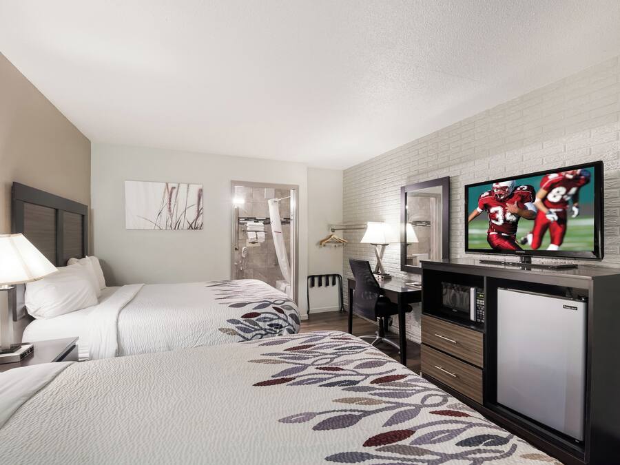 Habitació d'hotel amb dos llits, un escriptori, una televisió i un frigorífic.