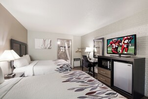 Habitación de hotel con dos camas, un escritorio, un televisor y un refrigerador.