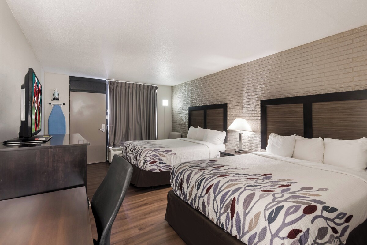 A hotel room with two beds, a desk, a chair, a TV, and a window with curtains.