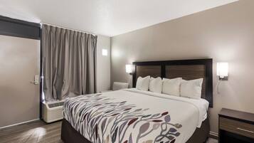 A hotel room with a large bed, a bedside table, a lamp, and a window with curtains.