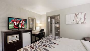 Habitación de hotel con cama, escritorio, televisor, microondas y zona de ducha.
