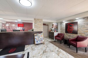 Zona de recepción de Red Roof Inn con piso de mármol, mostrador de recepción, estación de café y sillas de cuero rojo.