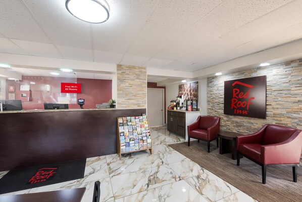 Zona reception di un Red Roof Inn, con pavimento in marmo, scrivania, angolo caffè e poltrone in pelle rossa.
