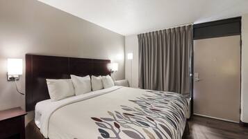 A hotel room with a large bed, a wooden headboard, a bedside table, a nightstand, and a window with curtains.