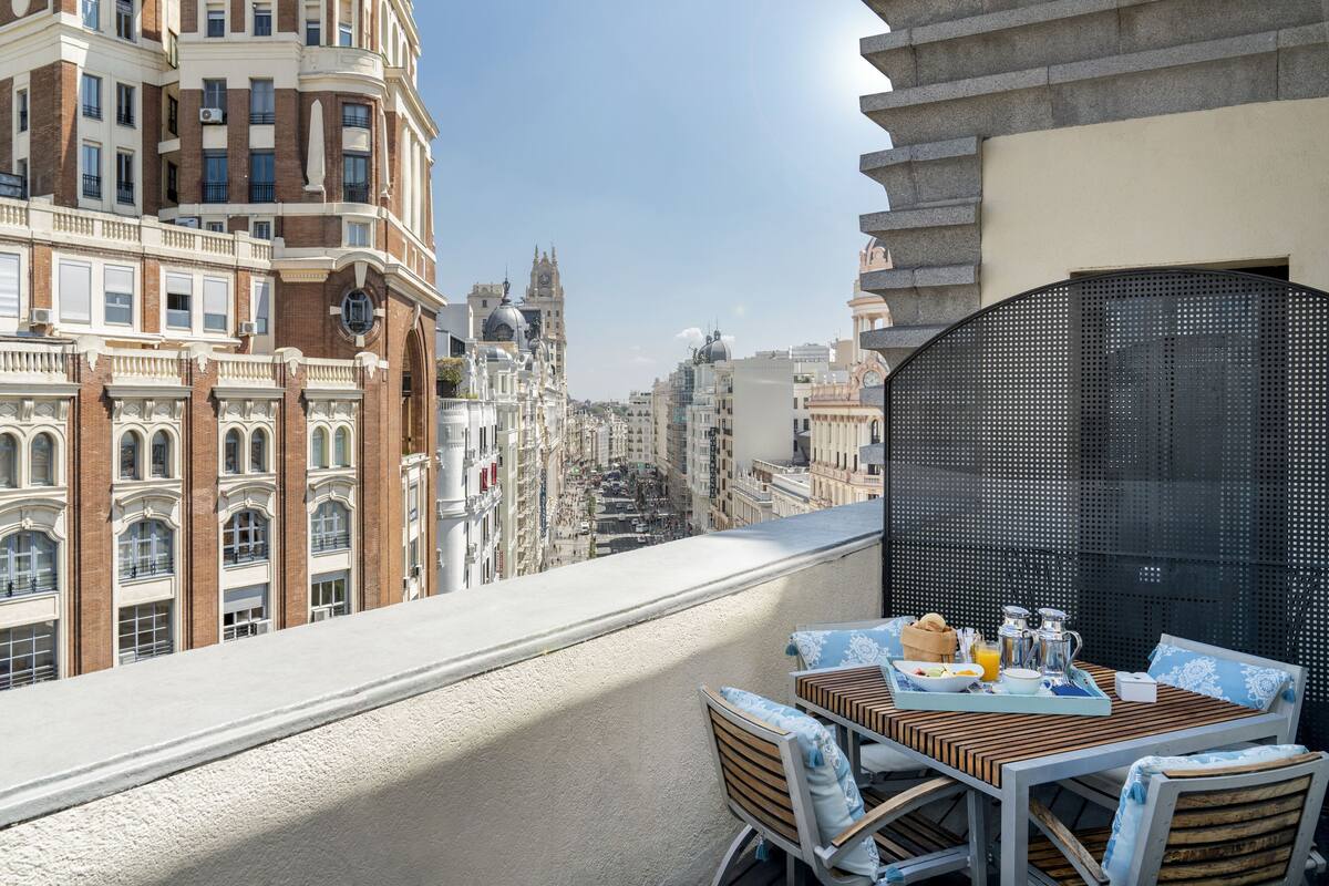 A balcony with a table set for breakfast, overlooking a cityscape with historic buildings.