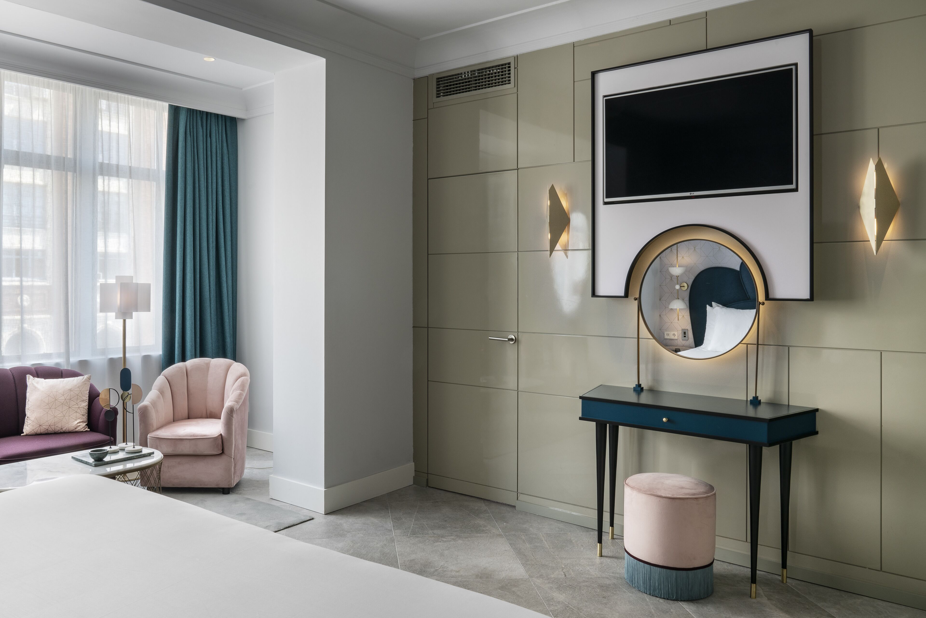 A modern bedroom with a large bed, a vanity with a mirror, and a seating area with a sofa and armchair.