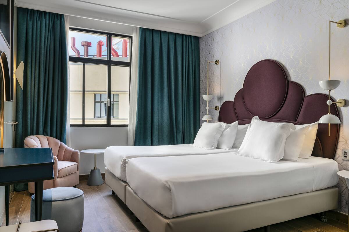 A hotel room with two beds, a desk, a chair, and a window with curtains.