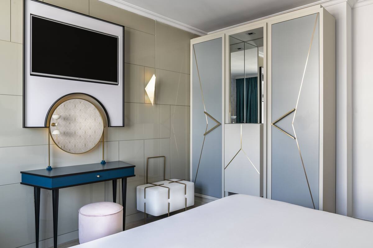A modern bedroom with a bed, a desk, a round mirror, a wardrobe, and a TV.