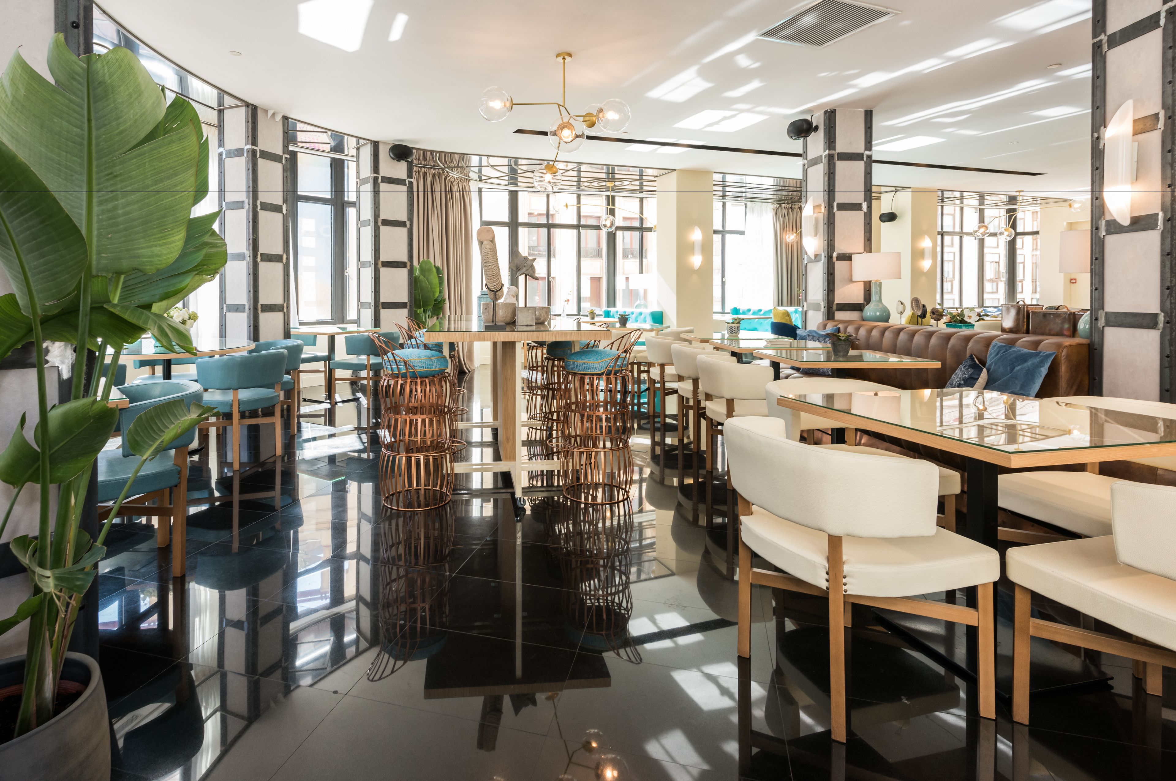 A modern hotel lobby with a curved glass wall, a central dining area, and a seating area with sofas and chairs.