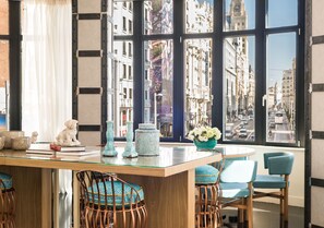 A modern dining area with a glass table, wicker chairs, and a view of a cityscape through large windows. - Hotel Vincci Capitol (Madrid)