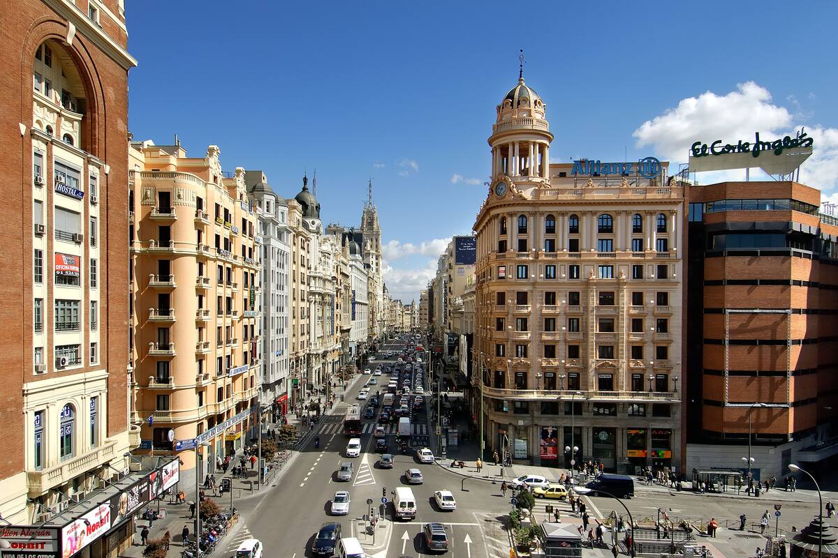 A busy urban street lined with historic buildings, including a prominent hotel with a clock tower.