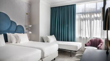 Een hotelkamer met twee bedden, een bureau, een stoel en een groot raam met gordijnen.