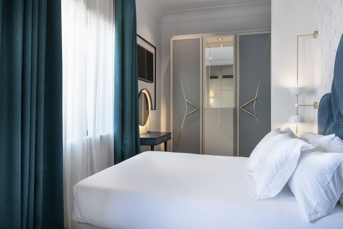 A hotel room with a bed, a desk, a mirror, and a wardrobe.