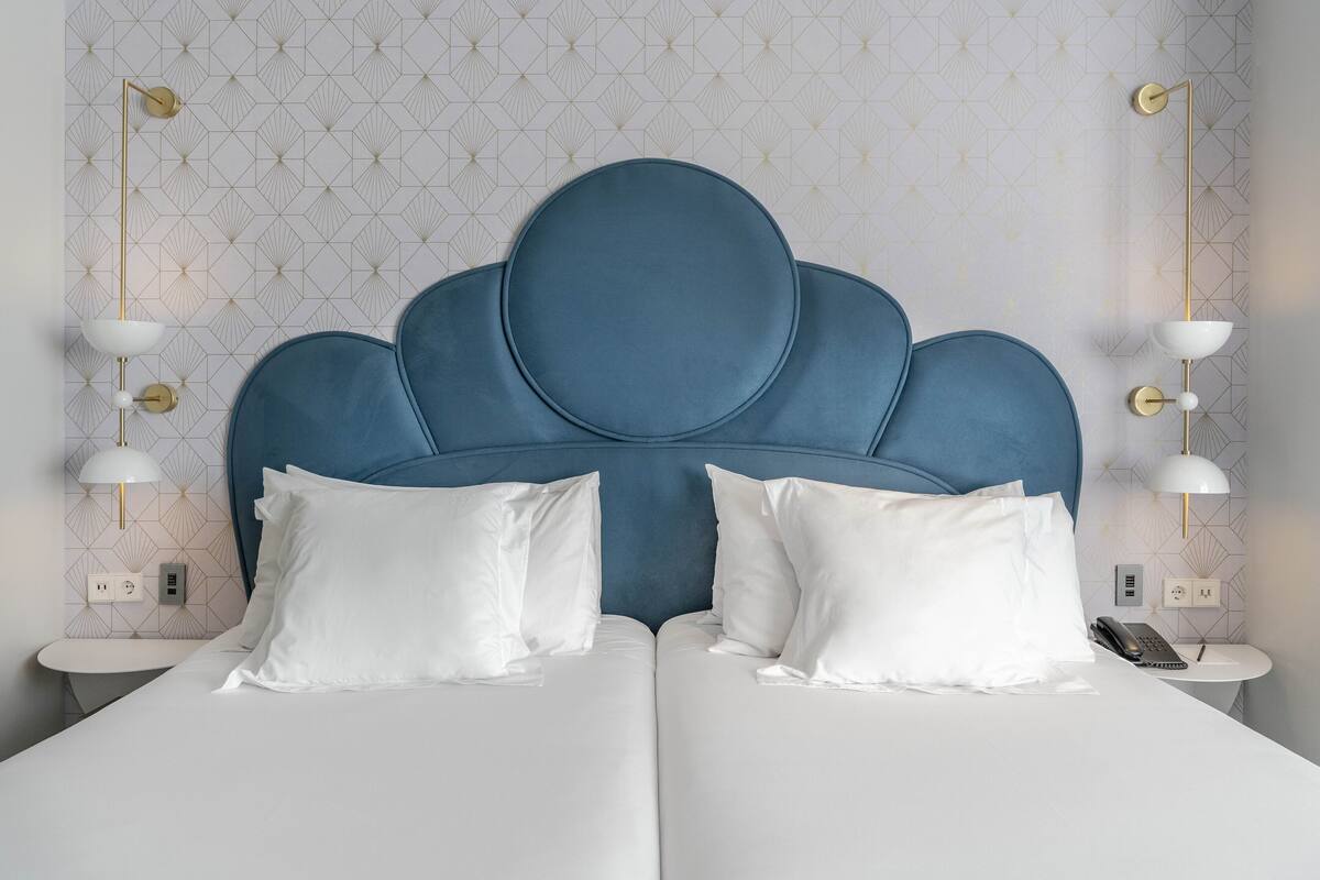A double bed with a blue upholstered headboard, white bedding, and two bedside lamps.