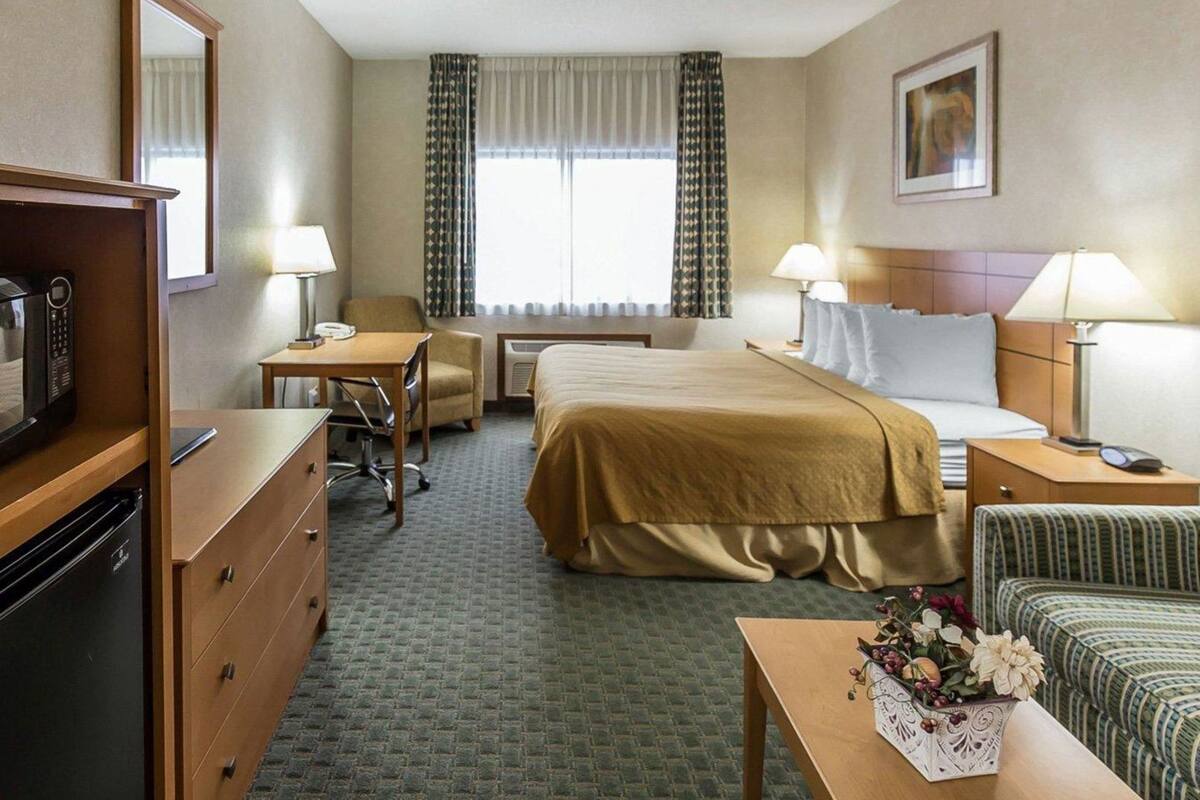 A hotel room with a bed, desk, chair, dresser, and a microwave.