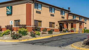 Ein Quality Inn Hotel mit beige gestrichener Fassade, einem überdachten Eingangsbereich und einem begrünten Vorgarten mit roten Blumen.