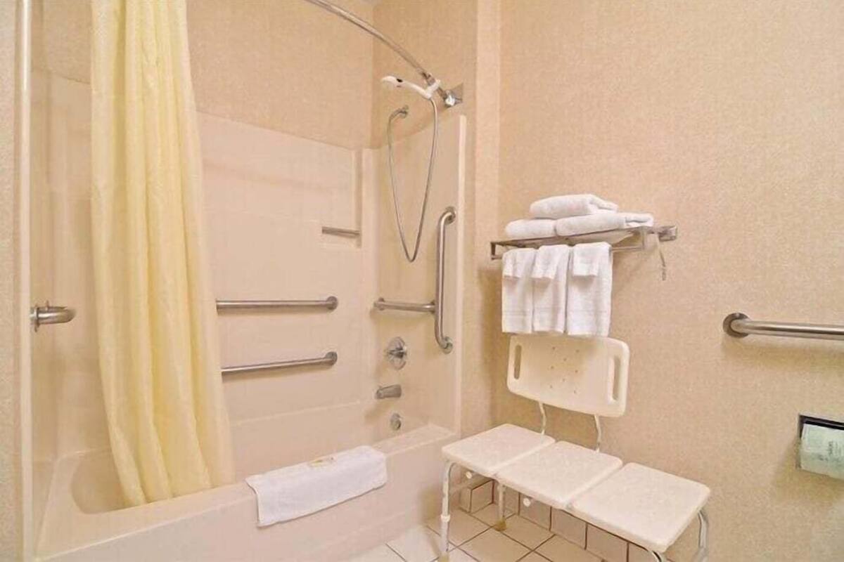 A bathroom with a bathtub, shower, handrails, a towel rack, and a bench.