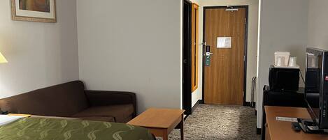 A hotel room with a bed, a desk, a chair, a sofa, a television, and a door leading to another room.