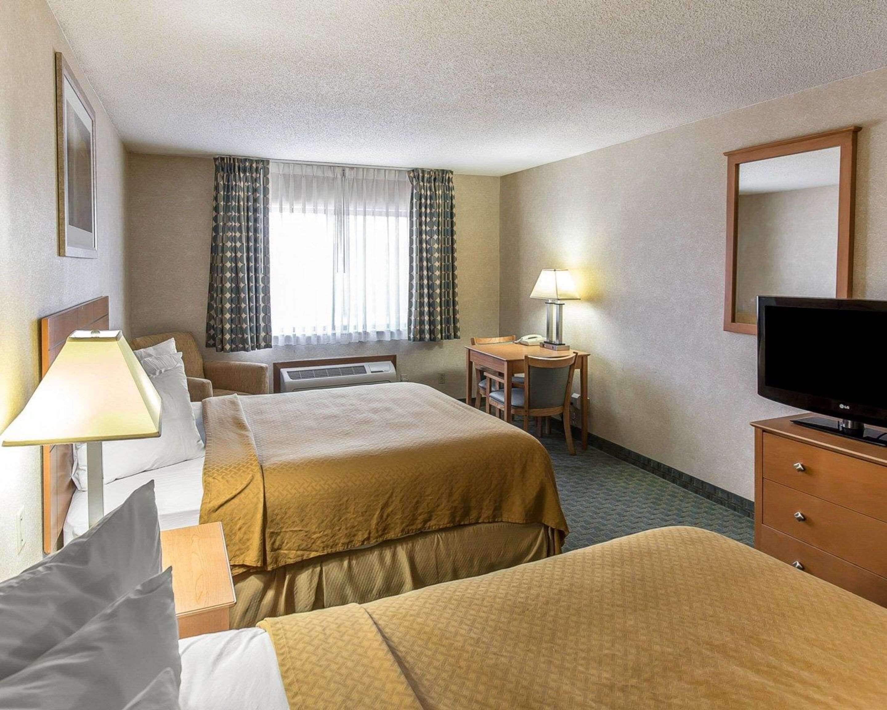 A hotel room with two beds, a desk with a chair, a TV, and a lamp.