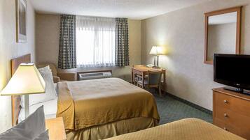 A hotel room with two beds, a desk with a chair, a TV, and a lamp.