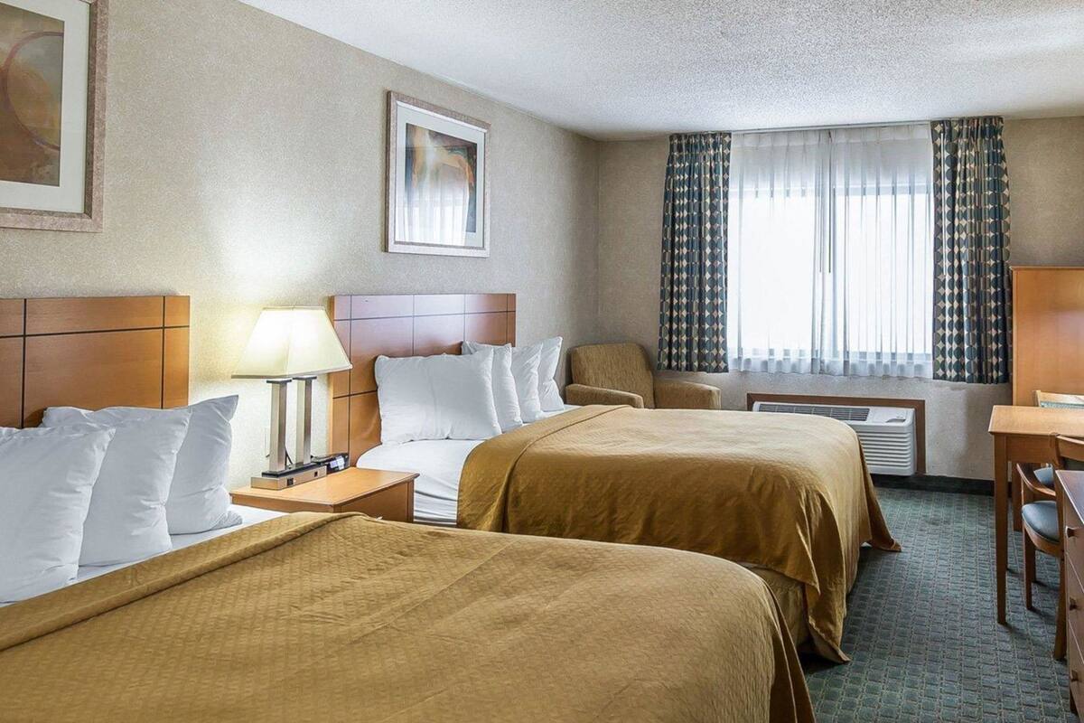 A hotel room with two beds, a desk, a chair, a lamp, and a window with curtains.