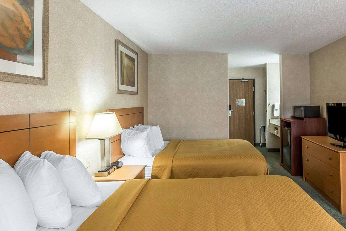 A hotel room with two beds, a desk with a lamp, a television, and a door leading to a bathroom.