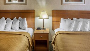 Ein Hotelzimmer mit zwei Betten, einem Nachttisch mit Lampe und zwei gerahmten abstrakten Gemälden an der Wand.