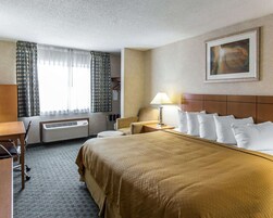 Habitación de hotel con cama, escritorio, silla, lámpara, un cuadro en la pared y ventana con cortinas.