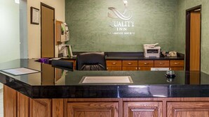 Ein Empfangsschalter mit grüner Wand, das Logo von Quality Inn by Choice Hotels und ein Holzkabinent mit Schubladen.