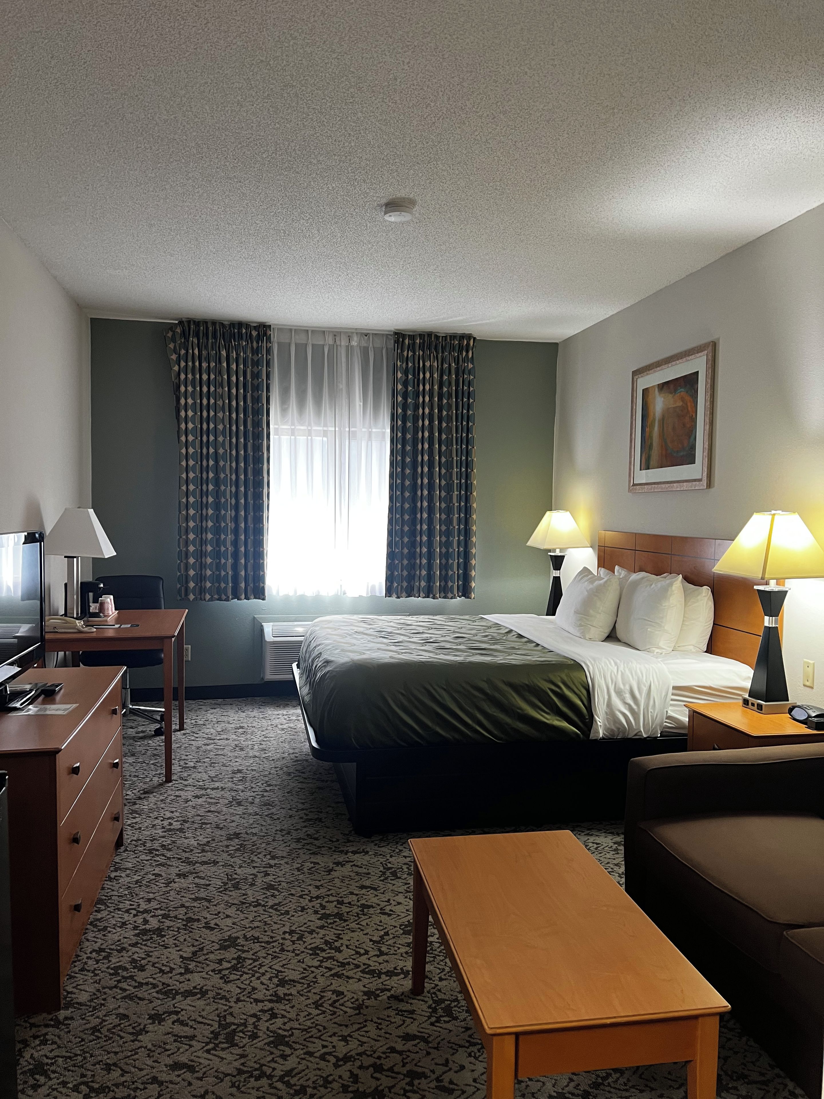 A hotel room with a bed, desk, chair, and a small table.
