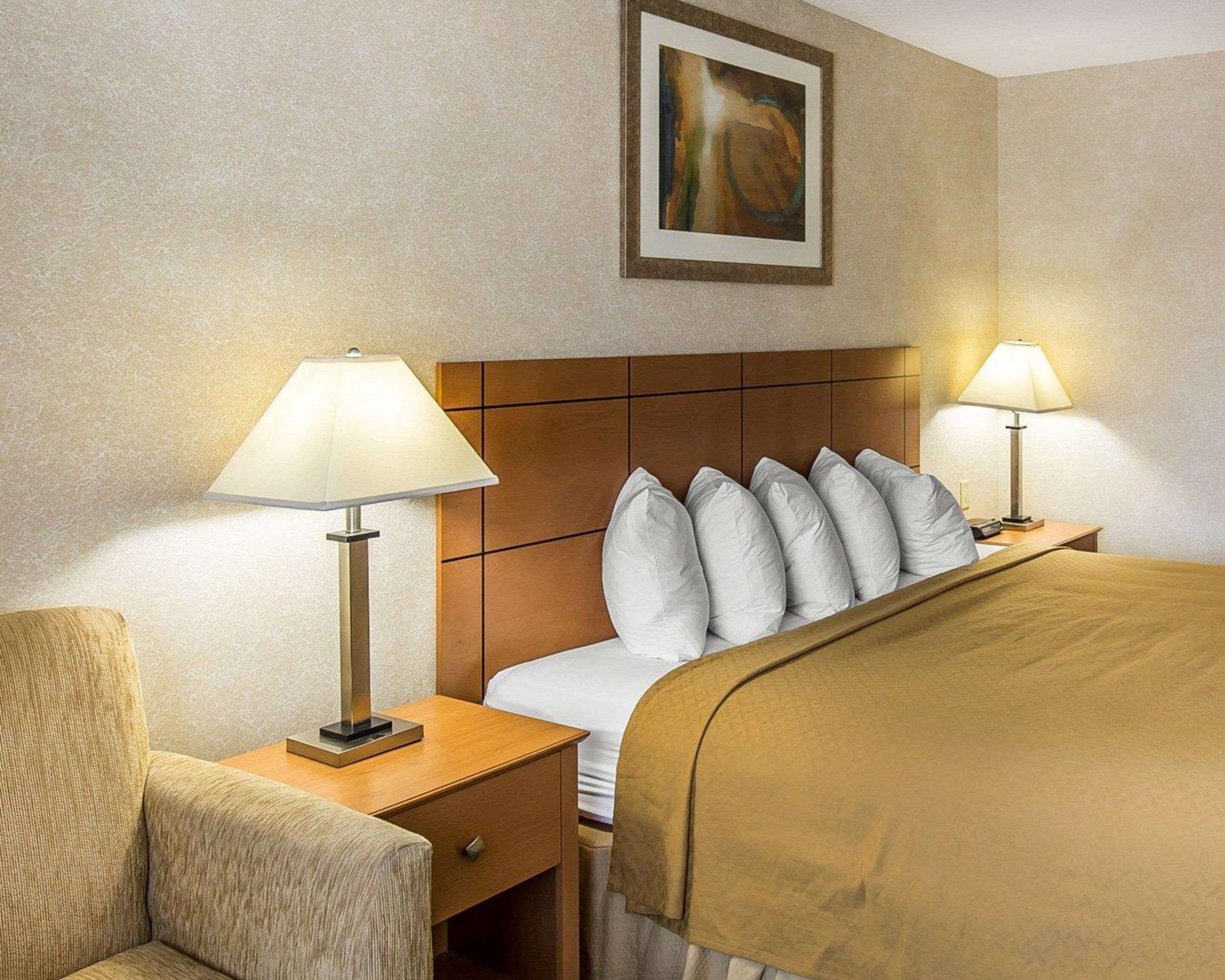 Ein Hotelzimmer mit einem Bett, zwei Nachttischlampen, einem Nachttisch, einem Sessel und einem Bild an der Wand.