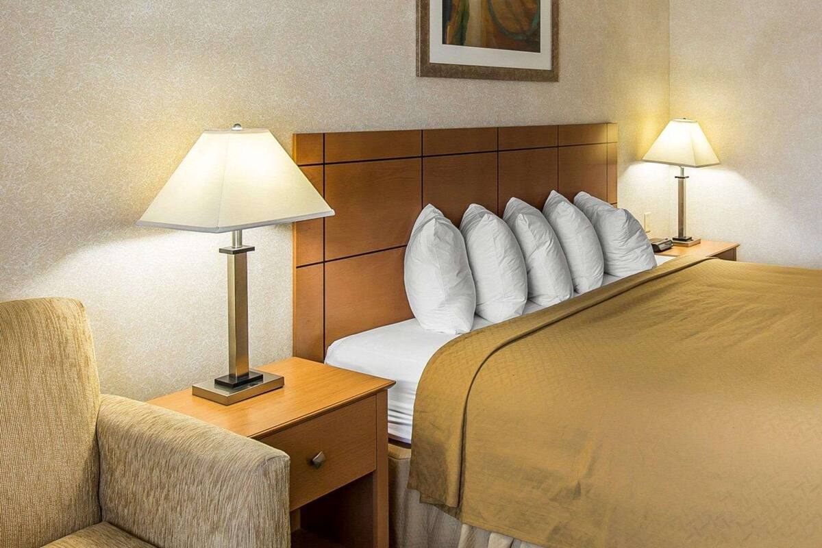 A hotel room with a bed, two bedside lamps, a nightstand, a chair, and a painting on the wall.
