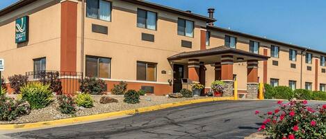 A Quality Inn hotel with a two-story structure, a covered entrance, and a landscaped front yard with flowers and shrubs.