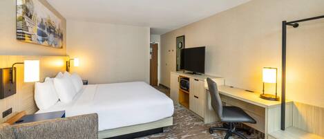 A hotel room with a bed, a desk, a chair, a TV, and a painting on the wall.
