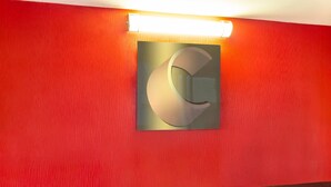 En röd vägg med ett stort, upplyst bokstavstecken i form av ett "C" och en rektangulär lamparmatur.