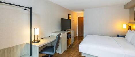 Ein Hotelzimmer mit Bett, Schreibtisch, Stuhl, Fernseher und einer Tür zu einem anderen Raum.