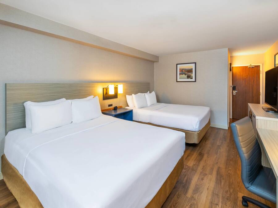 A hotel room with two beds, a desk, a chair, a television, and a framed picture on the wall.