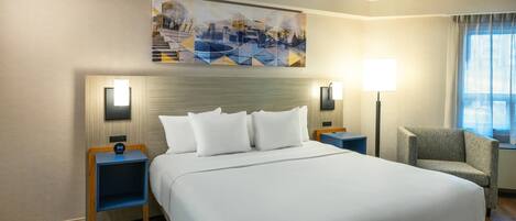 A hotel room with a large bed, two bedside tables, a chair, a painting on the wall, and a window with curtains.