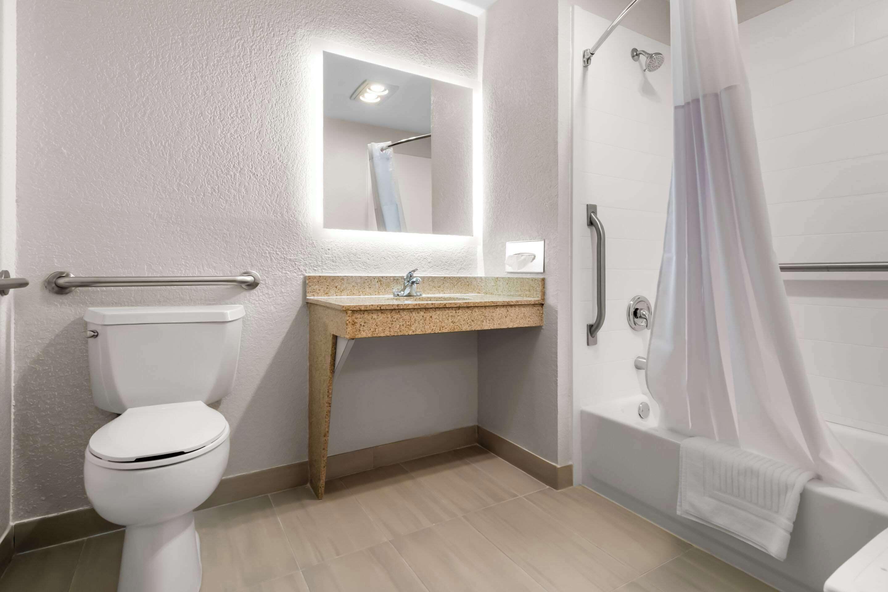 Un baño con inodoro, lavamanos, espejo, ducha y toallero.