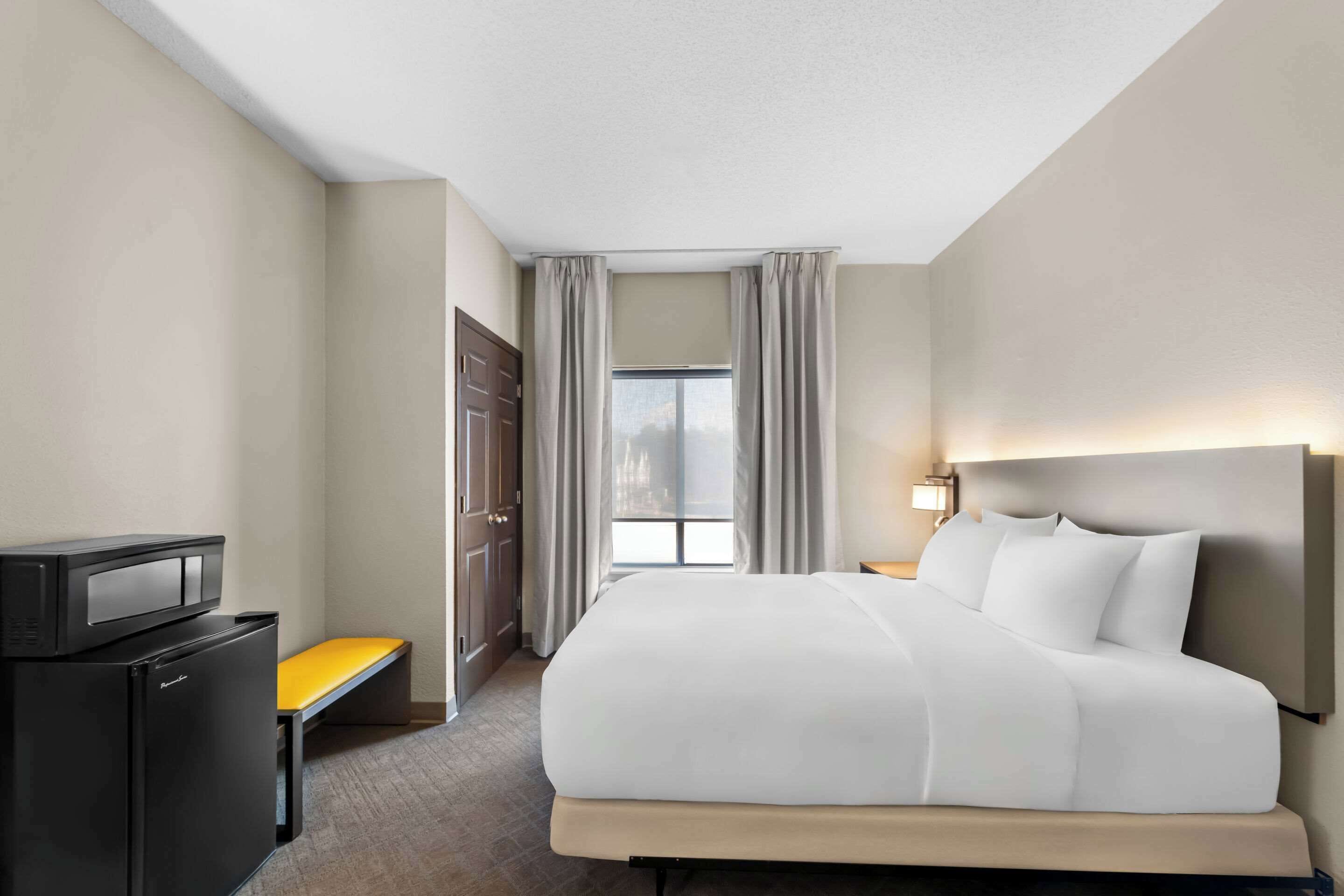 A hotel room with a bed, a desk, a television, and a window with curtains.