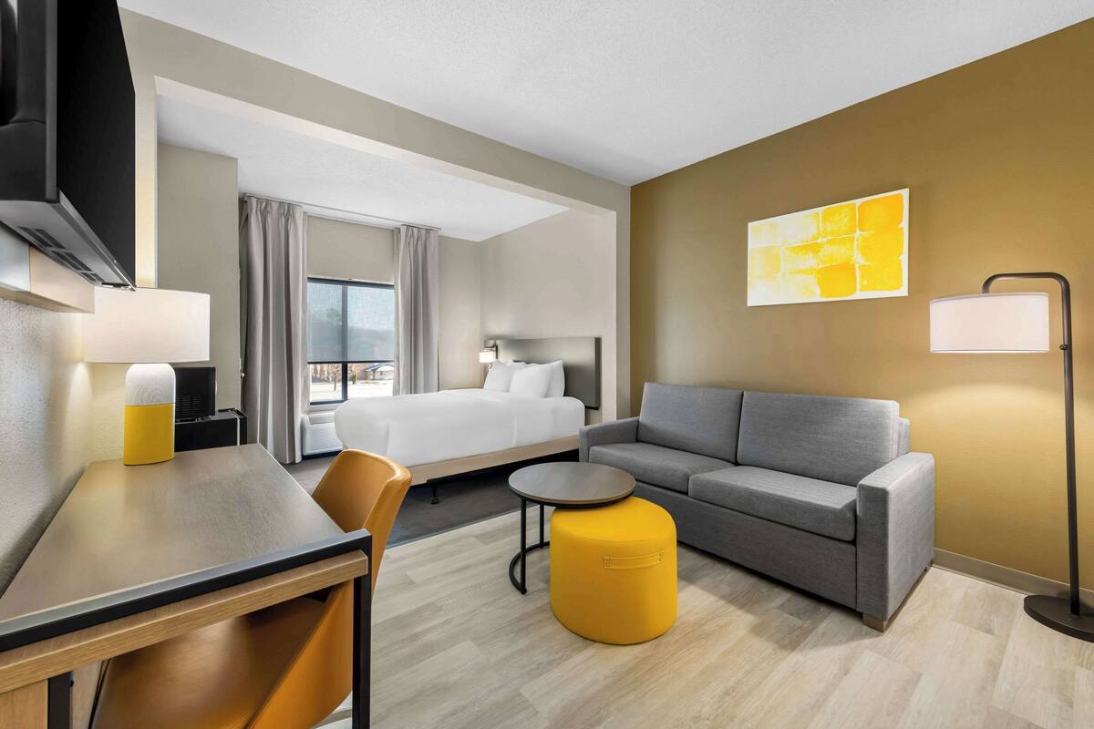 A hotel room with a bed, sofa, dining table, and chairs.