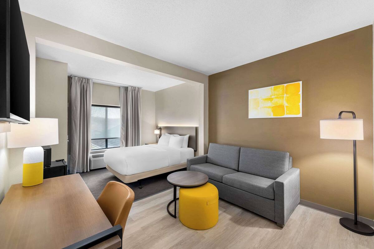 A hotel room with a bed, a sofa, a dining table, and a small round table.