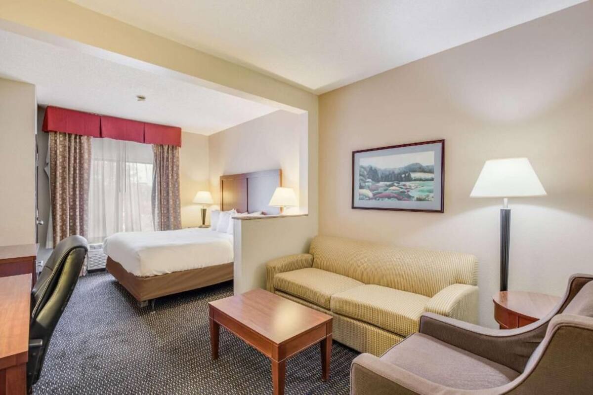 A hotel room with a bed, two bedside tables, a sofa, a chair, a desk, and a lamp.