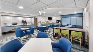 A modern hotel room with a dining area, a kitchen, and a TV mounted on the wall.
