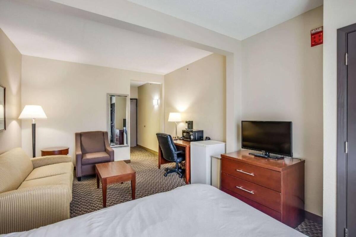 A hotel room with a bed, a desk with a computer, a chair, a TV, and a lamp.