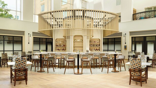 Un amplio vestíbulo de hotel con una zona de bar central, diversas disposiciones de asientos y un techo alto.