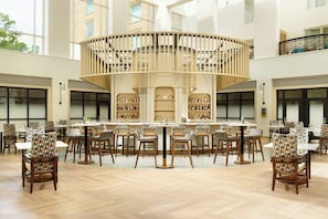 Eine geräumige Hotelhalle mit einer zentralen Bar, verschiedenen Sitzgelegenheiten und einer hohen Decke.