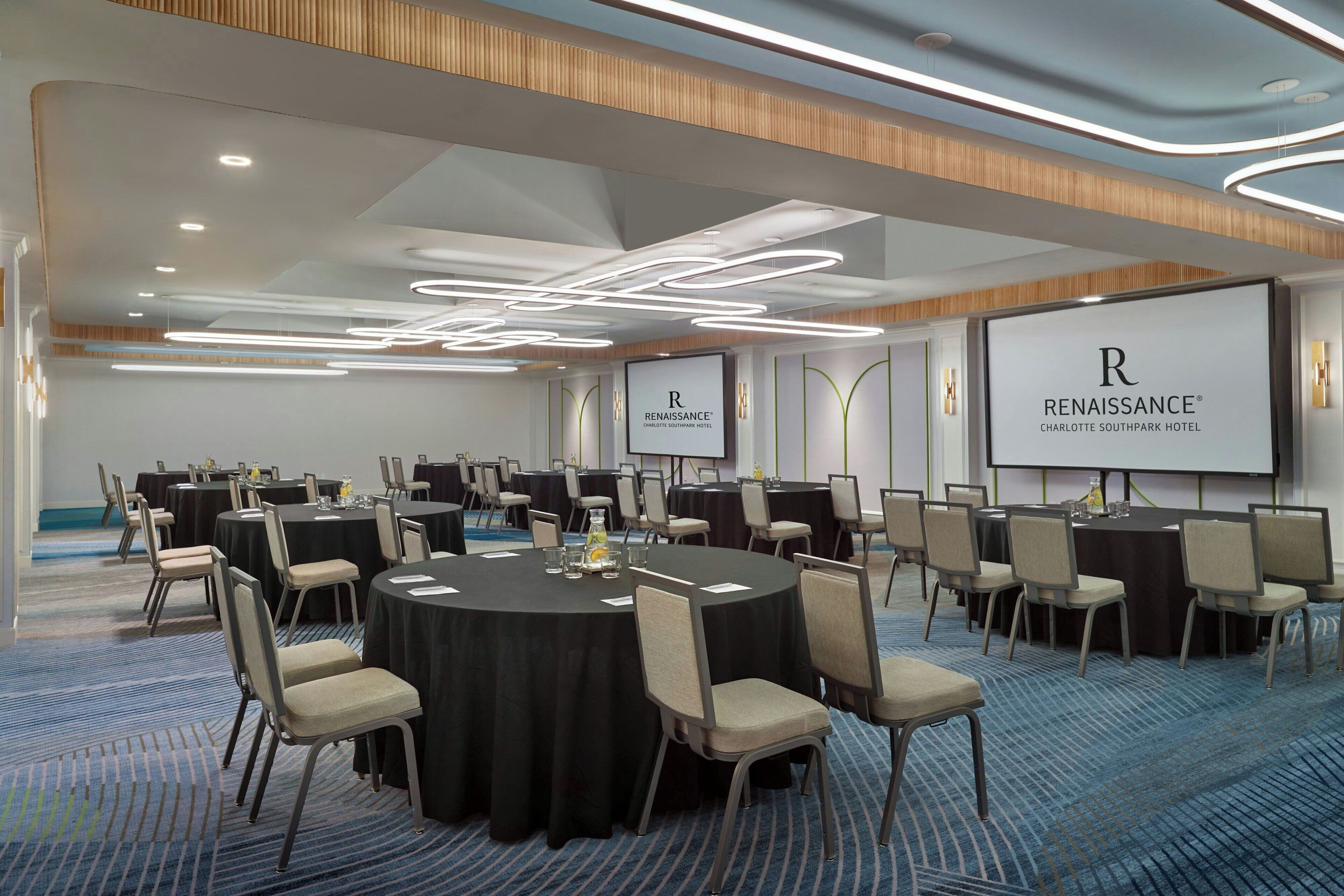 Una sala conferenze con diversi tavoli rotondi, sedie e schermi per presentazioni che mostrano il nome dell'hotel.