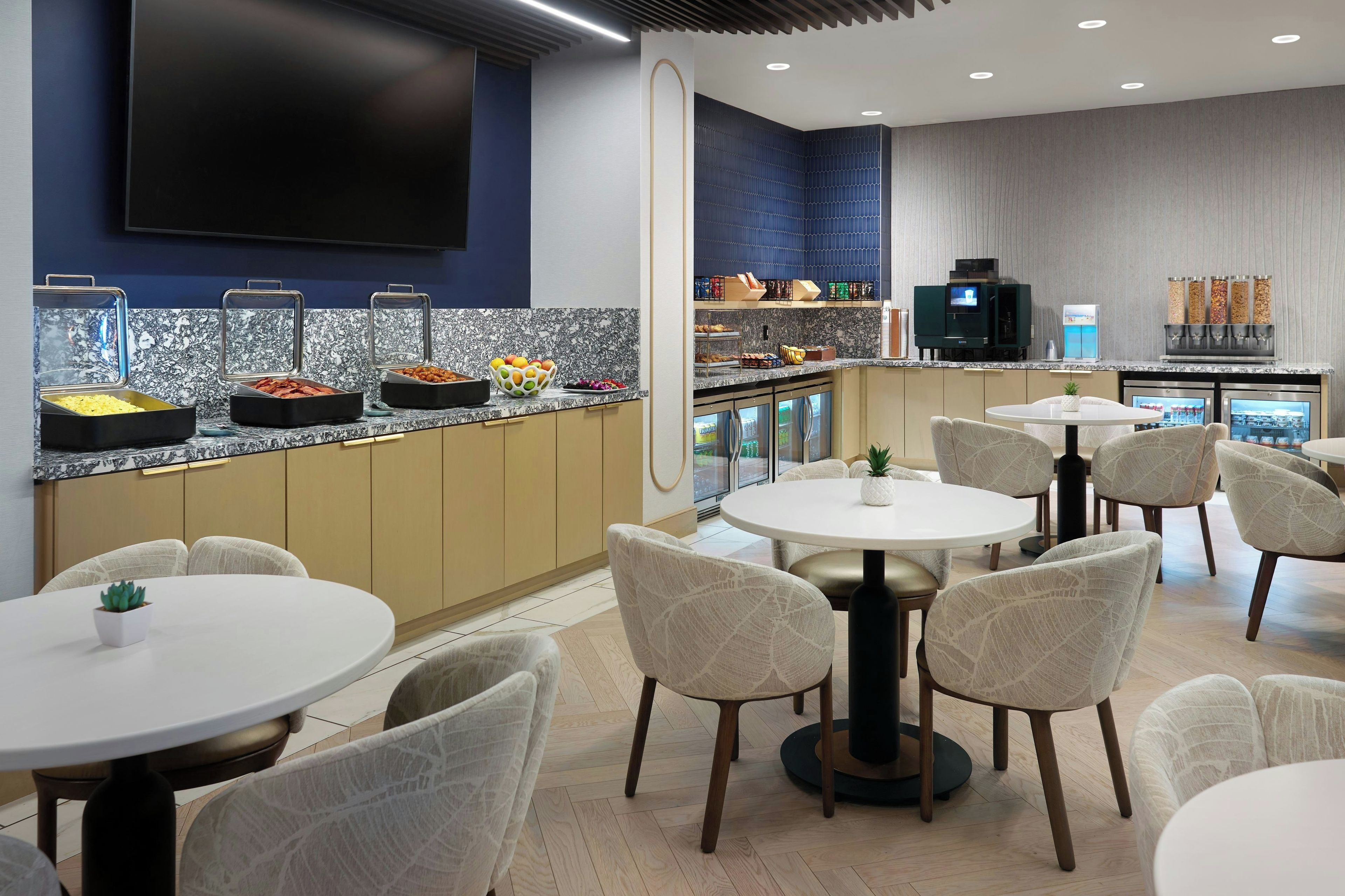 Une chambre d’hôtel moderne dotée d’un buffet pour le petit-déjeuner, d’un coin salon et d’une télévision à écran plat.
